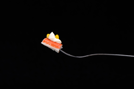 A piece of crab sticks with mayonnaise and corn on a fork isolated on black backgroundの写真素材
