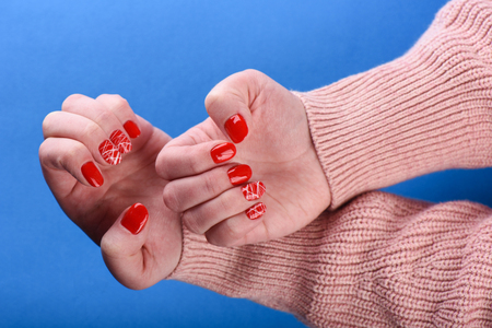 Hands of a girl in a beige sweater with a red manicure on her nails are isolated over a blue background.の写真素材