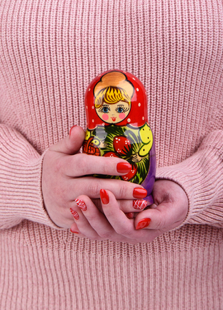Russian matryoshka in the hands of a girl in a beige sweater. Red manicure on the nails of the girl.の写真素材