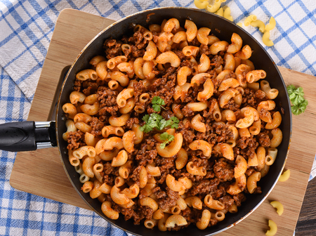 Top view. Makaroni po flotski russian national dish. Pasta with ground beef and tomato paste in a pan. Wooden table. Rustic styleの写真素材