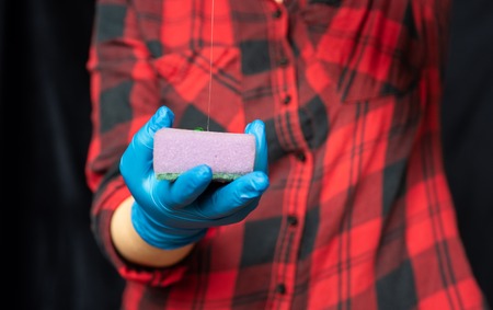 Girl pours detergent on the kitchen sponge. Hands of a girl in a hygienic gloves. The concept of cleanliness and health.の写真素材