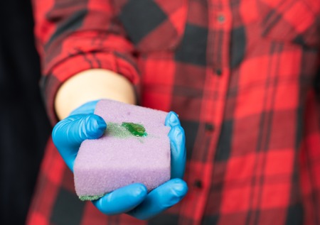 Kitchen sponge with a drop of cleaning agent. Hands of a girl in a hygienic gloves. The concept of...
