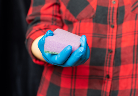 Kitchen sponge in the hand of the girl. Girl's hand in a hygienic glove. The concept of cleanliness and health.の写真素材