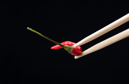 Chopsticks with red hot pepper pod isolated on black background. Copy spaceの写真素材
