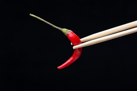 Chopsticks with red hot pepper pod isolated on black background. Copy spaceの写真素材