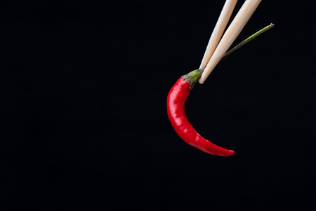 Chopsticks with red hot pepper pod isolated on black background. Copy spaceの写真素材