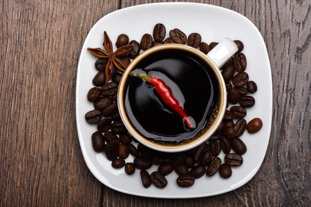 Hot pepper pod in a cup with hot coffee. Coffee beans and star anise on a saucer. Wooden background.の写真素材