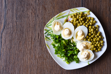 Boiled eggs are cut lengthwise and poured with mayonnaise. Green peas and green onions. A traditional russian dish. Rustic style. Copy space.の写真素材
