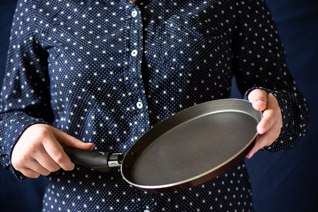 Pan in the hands of the girl. A girl with a pink manicure holding a frying pan. Close upの写真素材