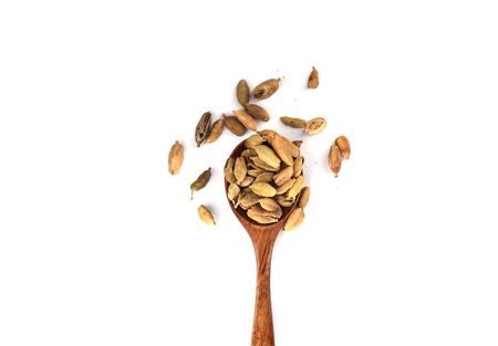 Cardamom seeds on a wooden spoon isolated on white background. Cardamom boxes are the seeds of an Indian tree from the ginger family. Copy space. Top viewの写真素材