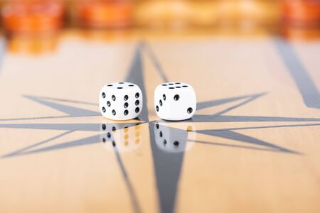 Dice and checkers on a wooden backgammon board. Game dice are reflected on the surface of the...