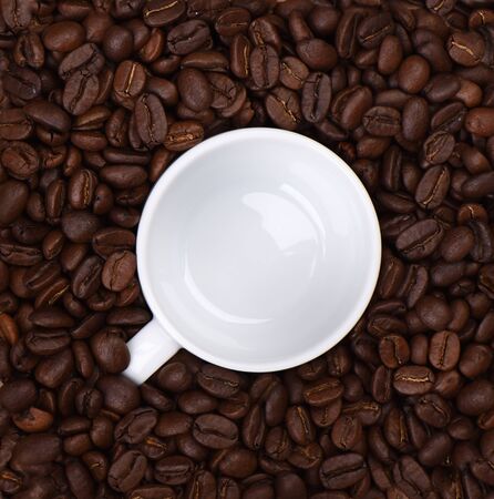 Empty coffee cup among coffee beans. Fragrant coffee beans and a coffee cup. Copy space. Close up.