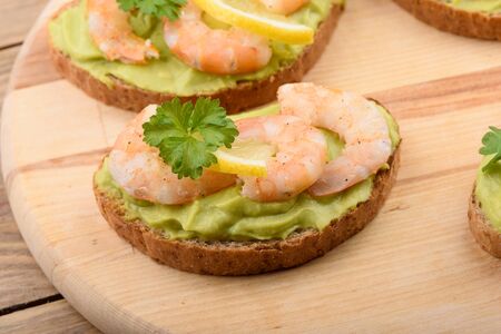 Sandwiches with avocado cream and shrimp on a cutting board. Multigrain bread, avocado cream, shrimp, lemon and parsley. Healthy eating.の写真素材