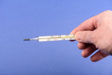 A glass mercury thermometer shows the high temperature of the human body on its scale. Human hand...