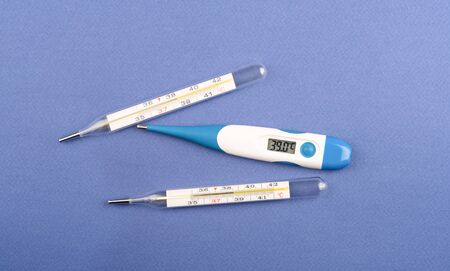 A glass mercury thermometer and an electronic thermometer indicate heat. Three body thermometers on...