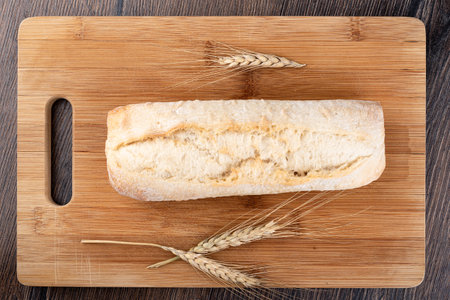 A whole ciabatta and a few dry ears of wheat on a cutting board. Top view. Close up.の写真素材