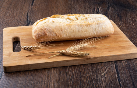 A whole loaf of ciabatta on a wooden cutting board. Several dry ears of wheat.の写真素材