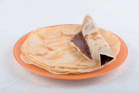 Rolled pancake with chocolate nut spread on a stack of pancakes. Close up.