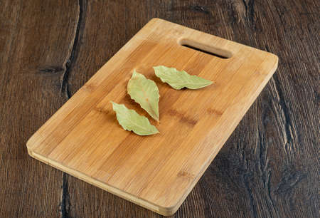 Three dry bay leaves on a wooden cutting board. Copy space.