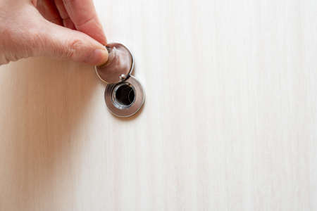 Human hand opens the peephole cover. Door furniture.