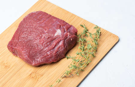 Raw beef on a wooden cutting board with thyme.