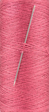 Full frame of red thread on spool and sewing needle in thread. Close up.