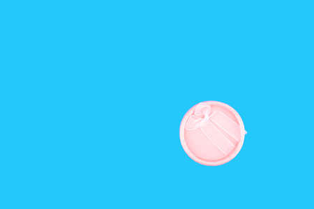 Round pink gift box with pink ribbon on a light blue background.