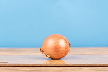 Unpeeled onion on a cutting board against a blue background. copyspace.の写真素材