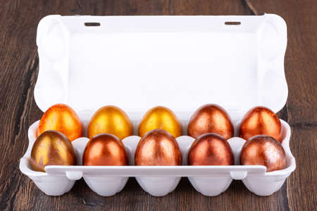 Painted in gold and bronze Easter eggs in a white plastic package on a wooden background.. Close up.の写真素材