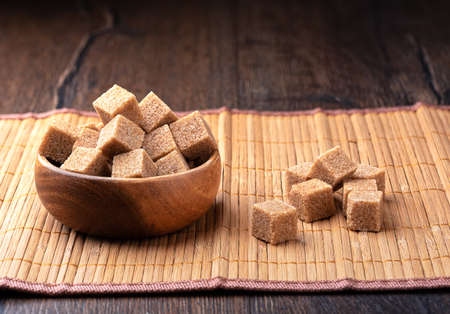 A wooden bowl full of cane sugar cubes and individual cubes on a food mat. copyspace.の写真素材