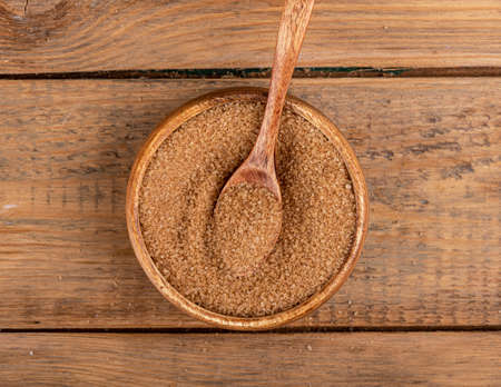 Top view of a wooden bowl with cane sugar and a wooden spoon.