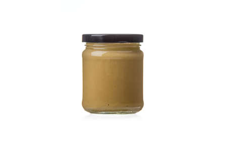 Closed glass jar with Dijon mustard on a white background. Black lead, copy space.