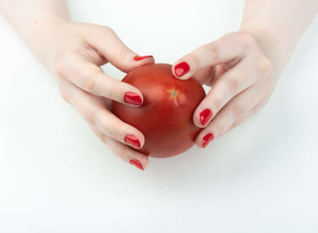 A woman's hand with nail polish is holding a red tomato. Manicure at home.の写真素材