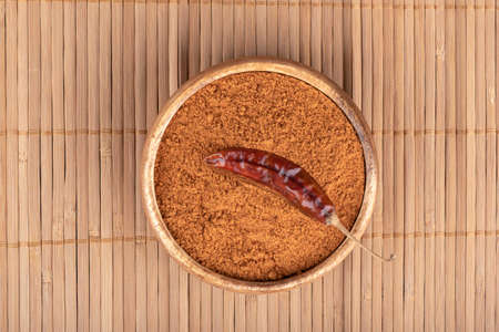 Hot pepper pod in a bowl with ground red pepper on a food mat. copyspace.