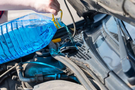 Woman hands pouring blue windshield washer fluid into a car's tank. close up.の写真素材