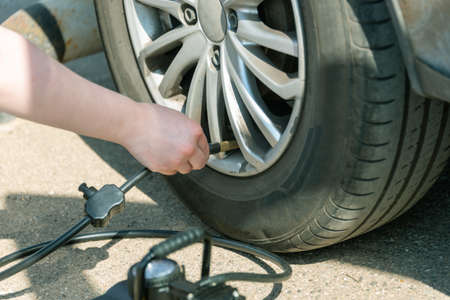 Connecting the compressor to the car tire, checking the air pressure and filling the car wheel with air. A woman's hand fastens a hose from a compressor to a car tire.の写真素材
