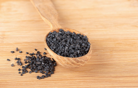 Black natural salt on a wooden spoon and wooden background. copyspace.の写真素材