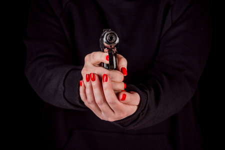 Womans hands with manicure hold a gun aimed at the viewer.の写真素材
