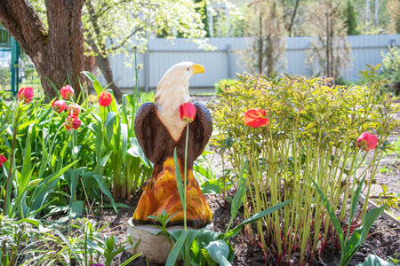 A flower bed in the yard of a cottage with an eagle figurine.の写真素材