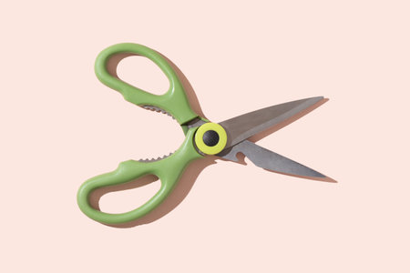 Opened kitchen scissors on a pale pink background with a hard shadow. Copy space.