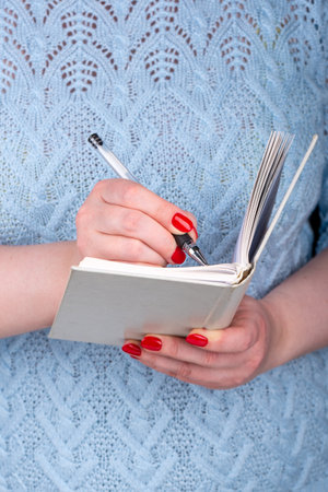 A young woman writes in a notebook or diary with a gel pen.
