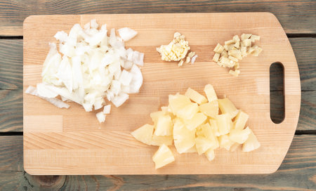 Chopped spices garlic, onions with ginger and pineapple pieces on a cutting board. Top view, wooden background.の写真素材