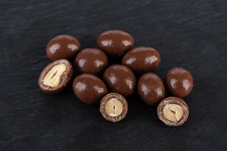 A few nuts whole and halves covered with dark chocolate on a stone surface.