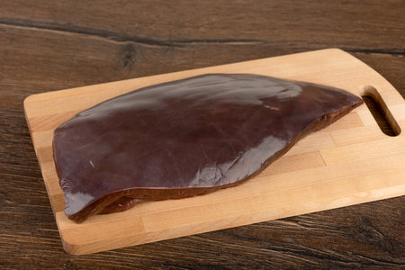 An uncut and unpeeled piece of beef liver on a cutting board. Cooking at home.