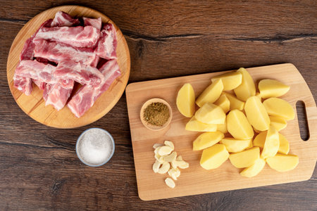 Top view of raw pork ribs, nom slices of raw potatoes, garlic slabs and spices on a cutting board. Home cooking.の写真素材