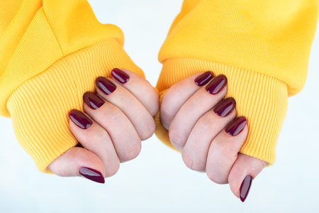Female hands in a yellow jacket with a blackberry-colored manicure on the nails. Copy space.の写真素材