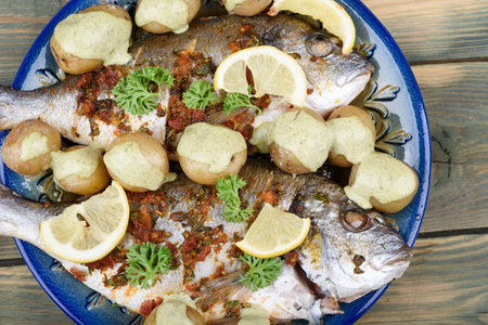 Baked dorado fish and baby potatoes on a plate with gremolata seasoning and cream sauce, garnished...