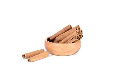 Cassia spice sticks in wooden bowl and on white background. Copy space.