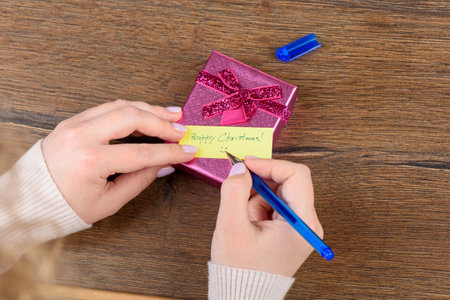 Handwritten note Happy Christmas on gift box, pen in female hands. Concept gifts.