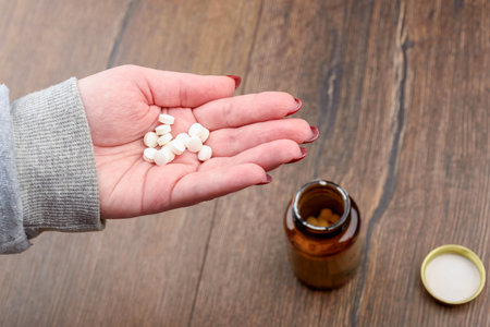 Close-up of female palm with medical pills on blurred glass bottle with pills background.